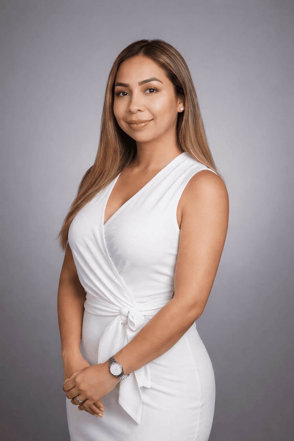 Woman with long highlighted hair wearing a white sleeveless wrap dress against a grey background.